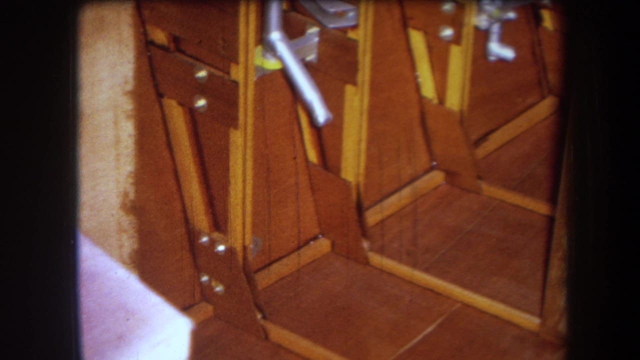1964 8mm frame showing a closer angle on the wooden apparatus, with exposed braces, metal fasteners, and a pale vertical board.