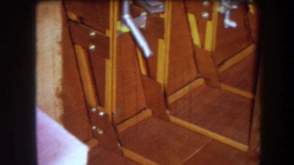 1964 8mm frame showing a closer angle on the wooden apparatus, with exposed braces, metal fasteners, and a pale vertical board.