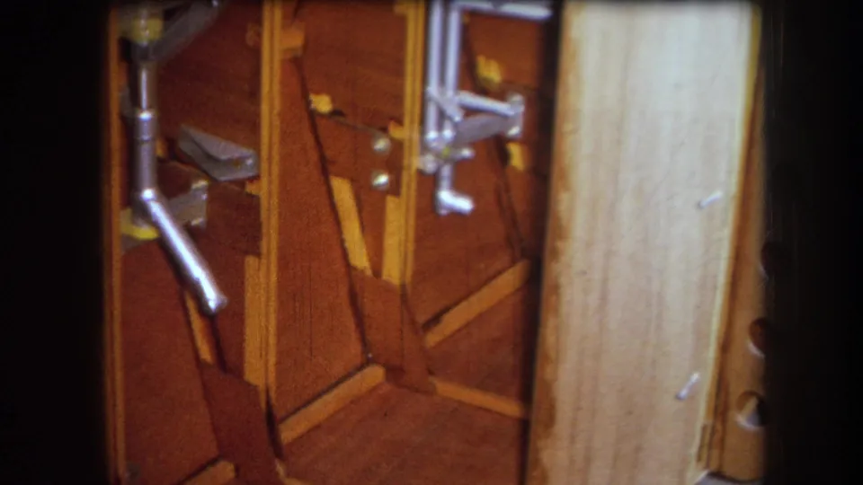 Final 1964 8mm frame showing the wooden mechanical interior, metal rods and brackets, angled braces, and a pale board at right.