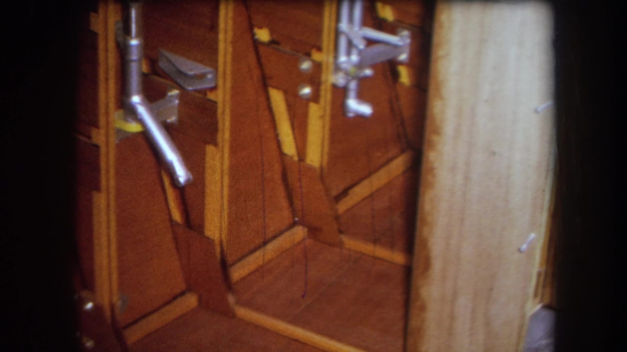 1964 Yucaipa home-movie frame showing brown wooden panels, angled trim, metal hardware, and a pale vertical surface at close range.