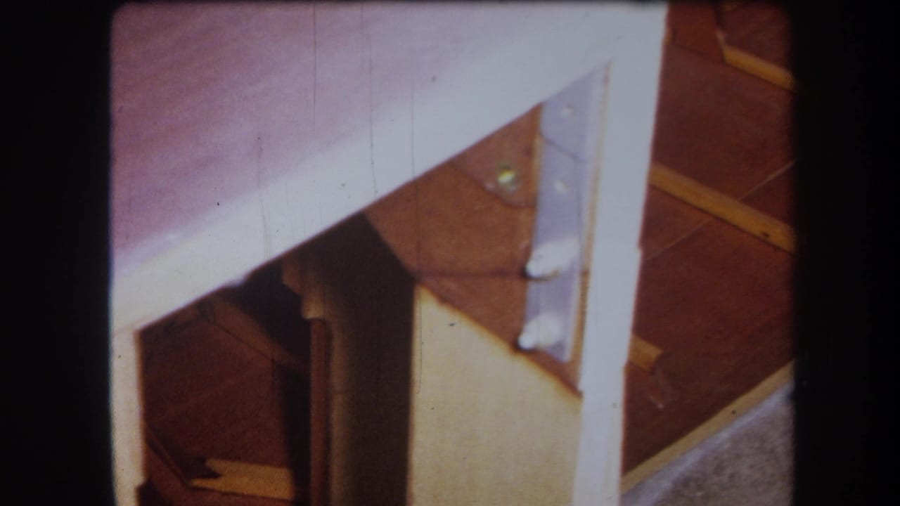 Close view under a wooden cabinet with pale panels, dark rails, and a metal support bracket.