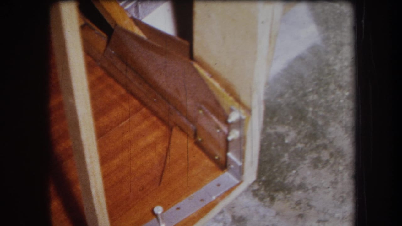 Close view of damaged wooden boards, metal brackets, pale trim, and gray flooring.
