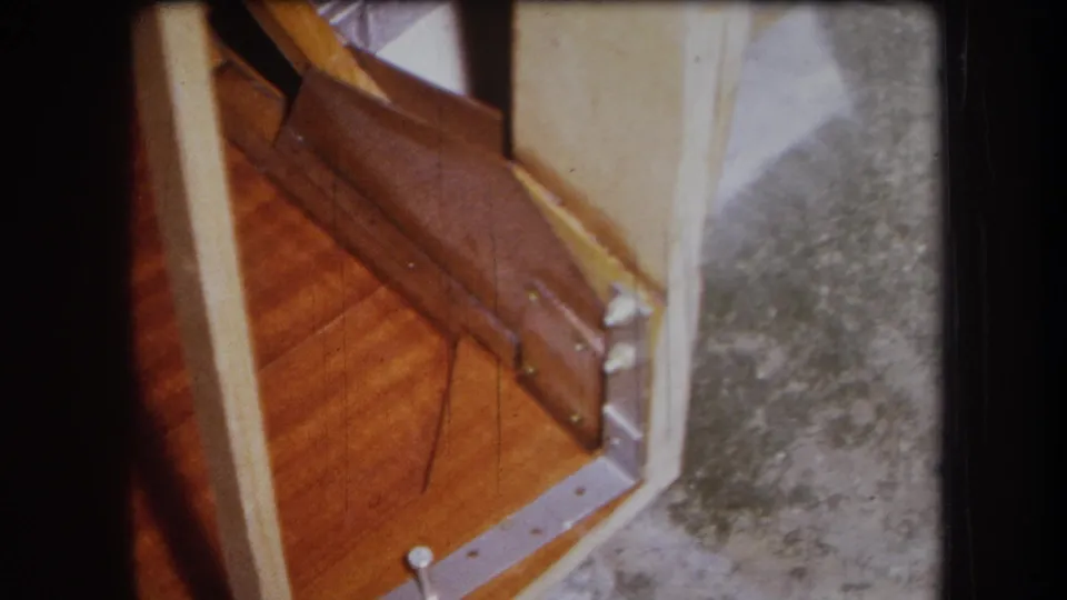 1964 8mm frame from the Yucaipa, California clip showing damaged wood near a threshold with metal hardware and gray floor surface.