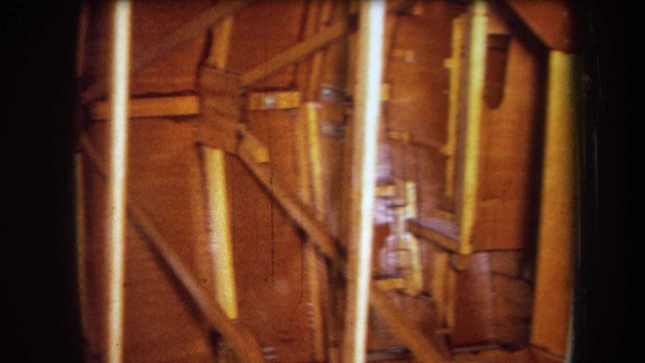 1964 Yucaipa-area 8mm frame showing amber-lit wooden rafters, diagonal braces, and vertical gate streaks inside an unfinished interior.