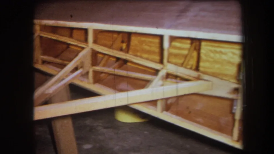 1964 Yucaipa home-movie frame showing a side section of wall framing with diagonal bracing and warm-toned panel surfaces.