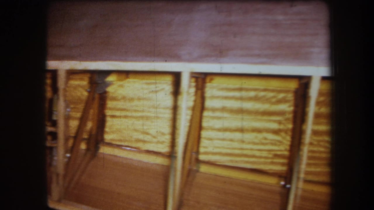 1964 Yucaipa-area home-movie frame showing wood ceiling panels, posts, diagonal bracing, and dark 8mm gate edges.