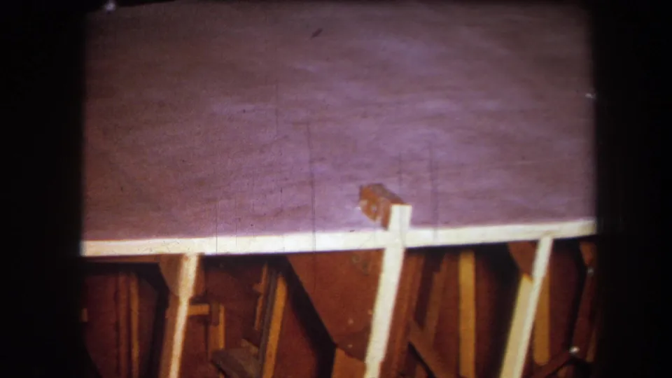 1964 Yucaipa home-movie frame showing the wooden structure from a slightly shifted angle, with a small cable or object near the upper edge.