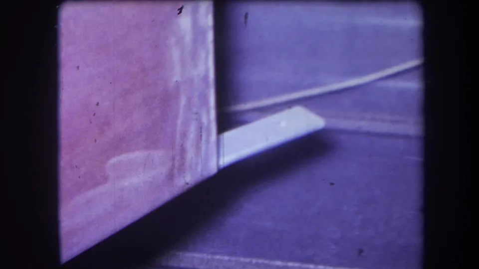 1964 Yucaipa 8mm frame showing a white rectangular object extending from a pink-purple corner surface with shadowed floor area.