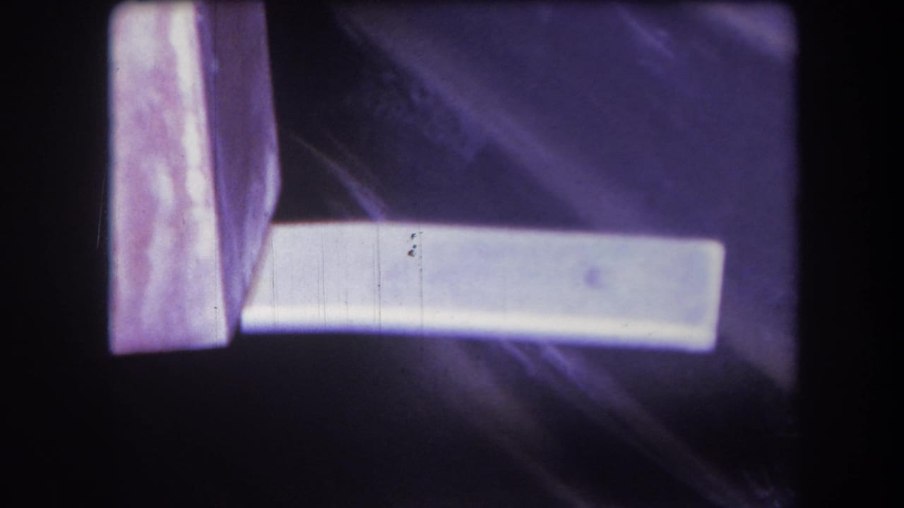 1964 Yucaipa 8mm frame showing a white plank crossing a purple-toned surface, with soft focus, scratches, and dark film borders.