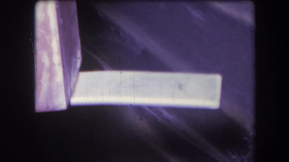 1964 Yucaipa 8mm still showing a white board or plank near the edge of a purple surface, with visible dust, scratches, and slight blur.