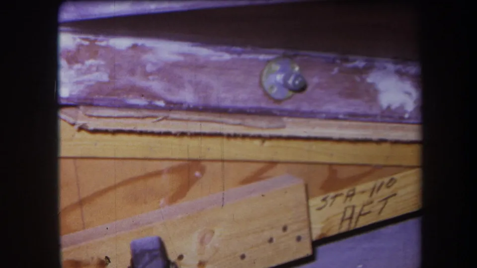 1964 8mm close-up from Yucaipa-area footage showing varnished wooden pieces, a round metal screw head, nails, and handwritten STA-110 AFT-style notation.