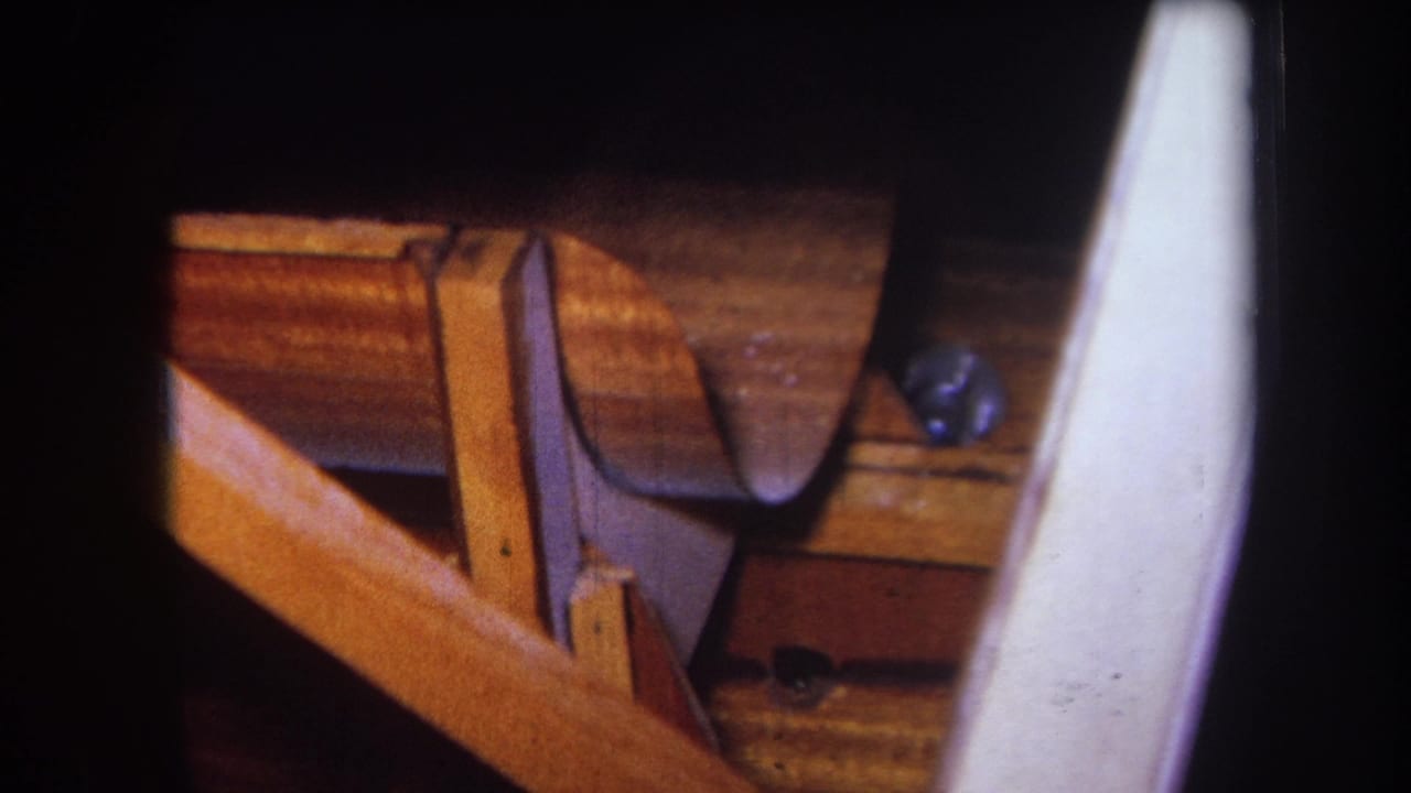 1964 Yucaipa woodshop close-up showing a curved wooden piece, bench structure, wood grain, and a pale foreground element.