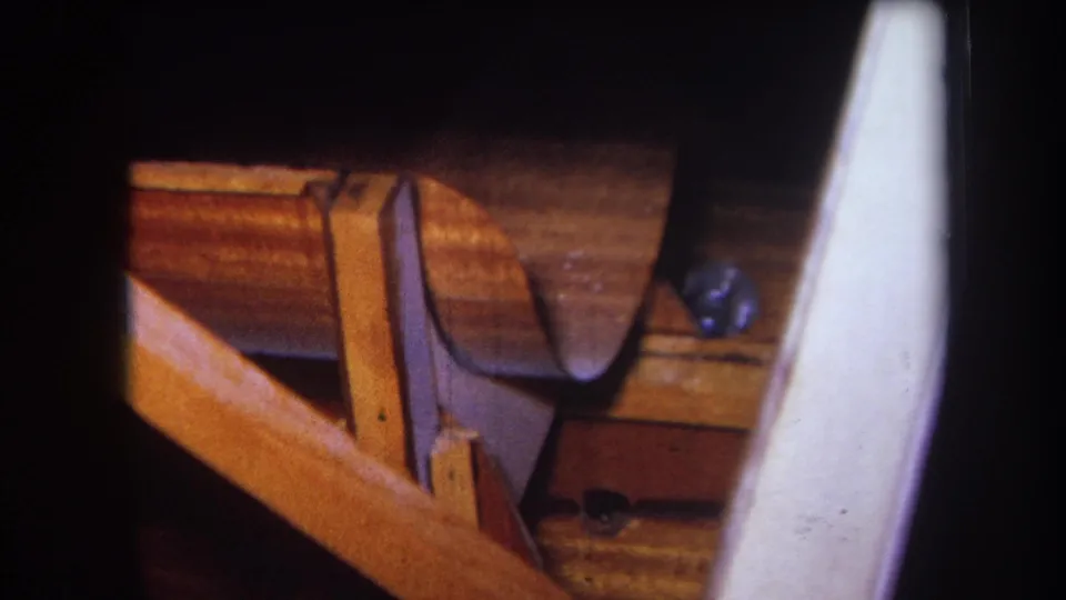 1964 Yucaipa woodshop close-up showing a curved wooden piece, bench structure, wood grain, and a pale foreground element.