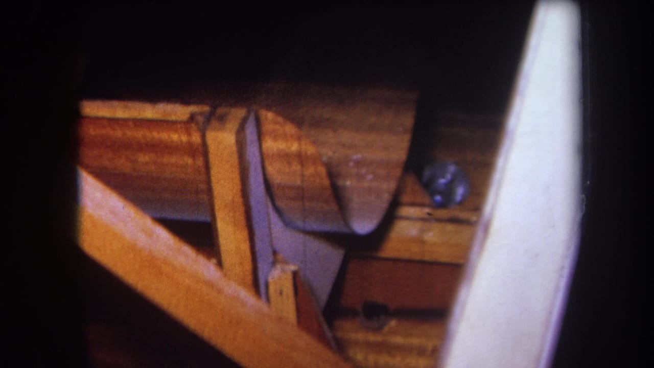 Similar close-up of a curved wooden section resting near bench supports and a pale foreground shape.