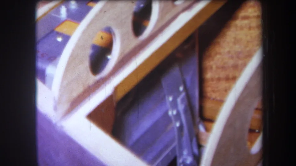 1964 Yucaipa workshop detail showing a wooden frame with drilled holes, a metal clamp-like part, and curved or stacked wood pieces.