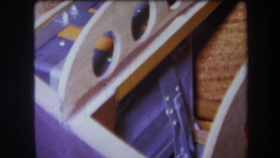 1964 Yucaipa home-movie frame showing an angled detail of wood, purple-painted metal, circular cutouts, and reflective fixture parts.