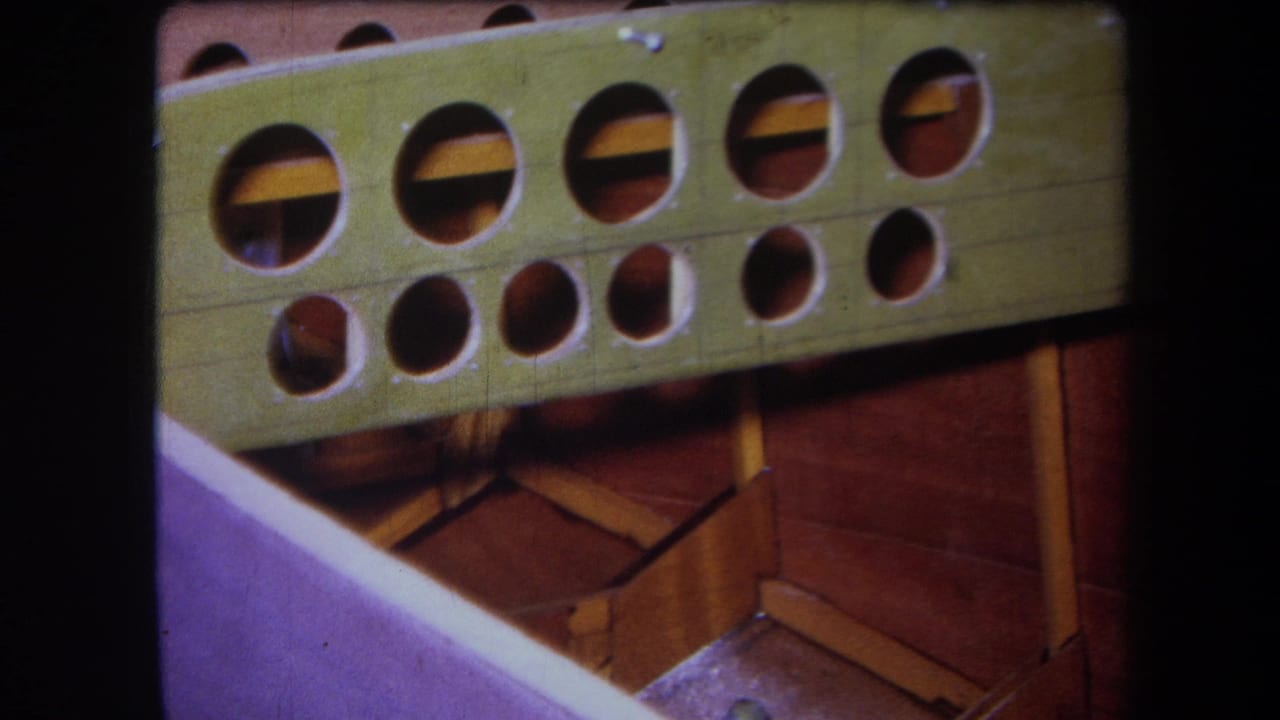 1964 Yucaipa boat-construction frame showing a green drilled member, exposed wooden supports, and a purple-painted edge.