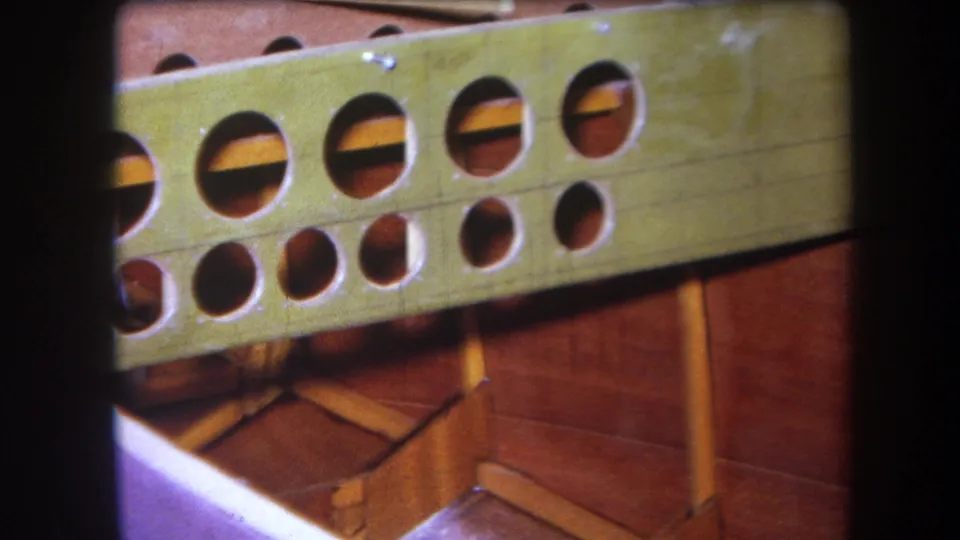 Close 1964 Yucaipa view of a green drilled structural piece, wooden boat framing, and purple-painted foreground surface.