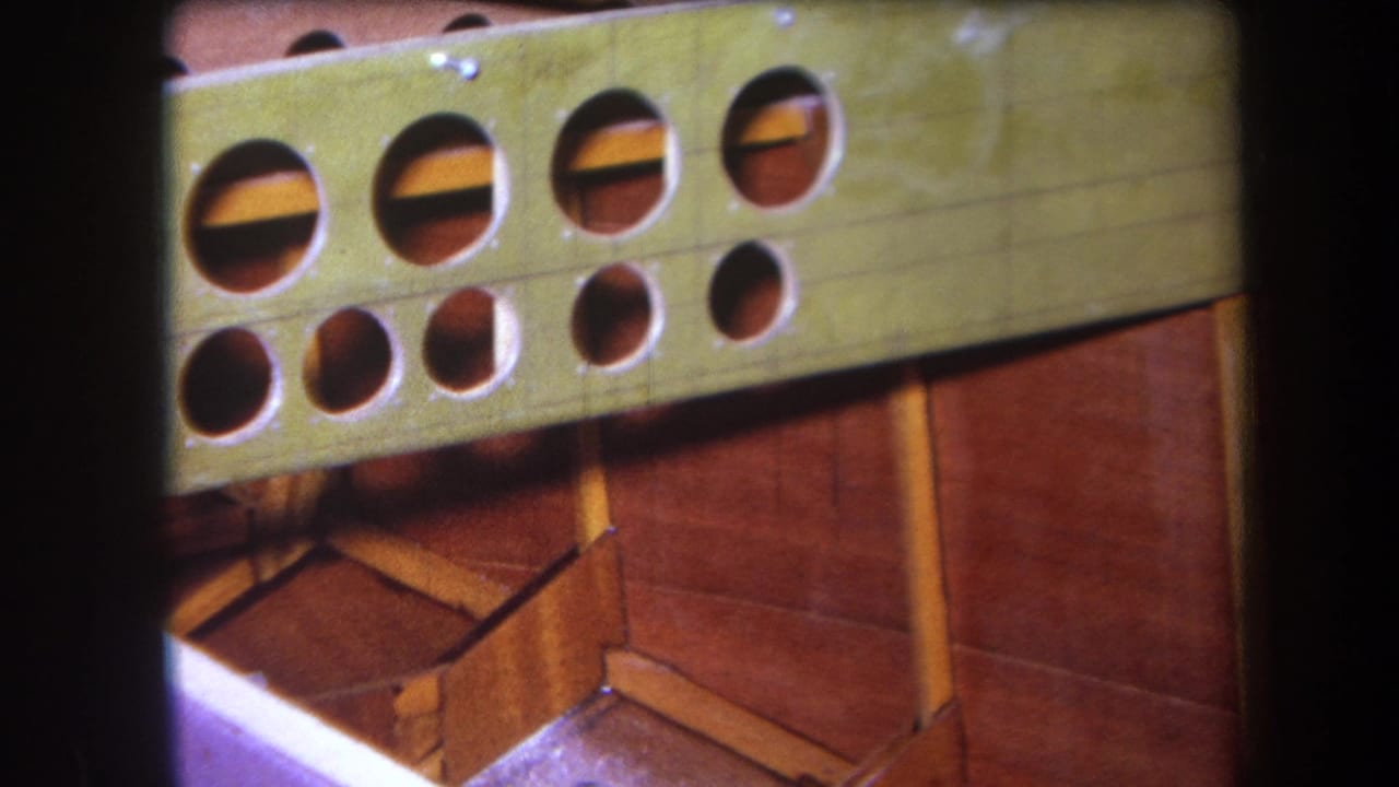 1964 Yucaipa 8mm frame showing a green painted wooden structure with rows of circular holes and reddish wood below.
