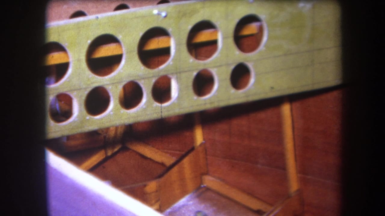 Close 8mm view of a green painted wooden object with circular cutouts, screws, and reddish structural pieces visible behind it.
