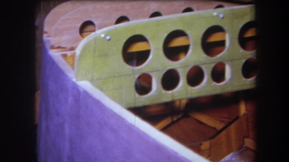 Final 8mm frame showing a pale curved edge next to a green wooden structure with round holes and reddish wood supports in Yucaipa, 1964.