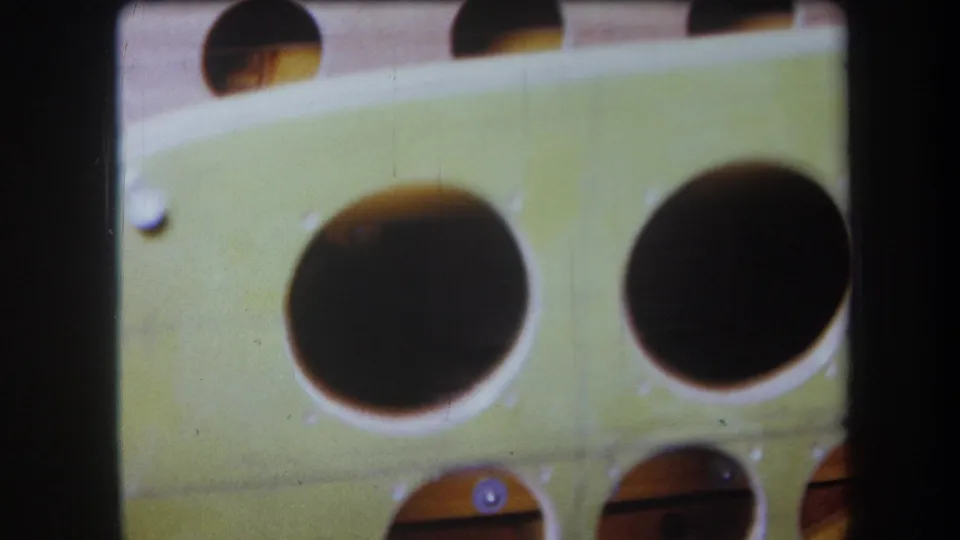 Soft-focused 1964 8mm frame showing two large circular cutouts in a green painted wooden panel with smaller openings below.