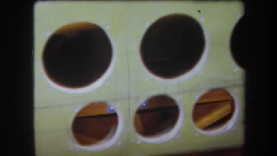 Final 8mm frame from the Yucaipa clip showing the green wooden panel face, paired large cutouts, lower holes, screws, and inner wood pieces.
