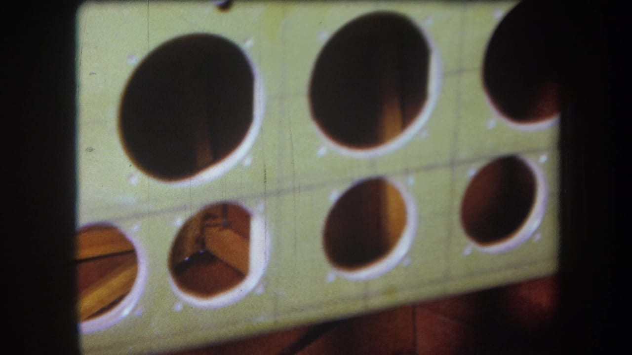 1964 Volmer Yucaipa frame with an angled view of a pale green board, round openings, darker cavities, and 8mm film texture.