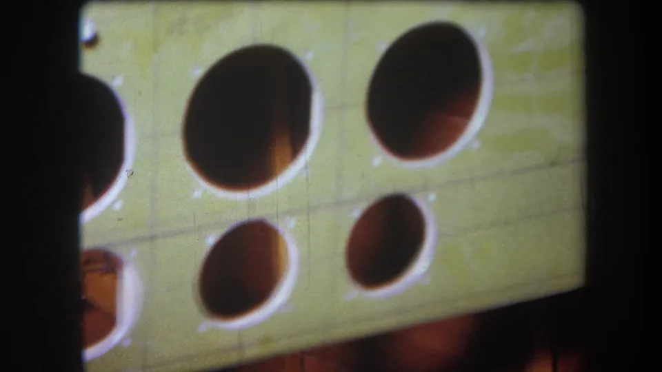 1964 Volmer Yucaipa close-up showing cropped circular cutouts in a pale green board with grain, scratches, and shadowed depth.
