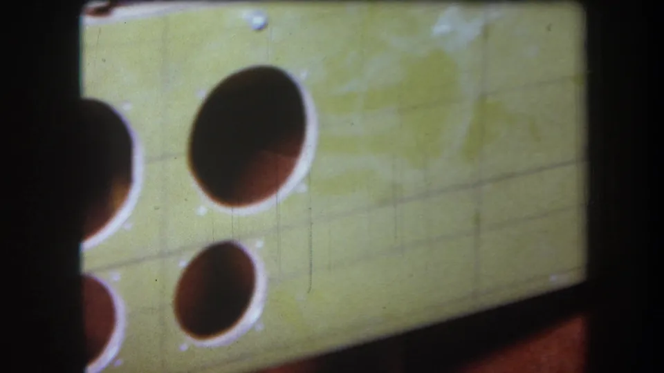 1964 Volmer Yucaipa frame showing a tilted pale green board with circular cutouts, shadowed interiors, and visible 8mm grain.