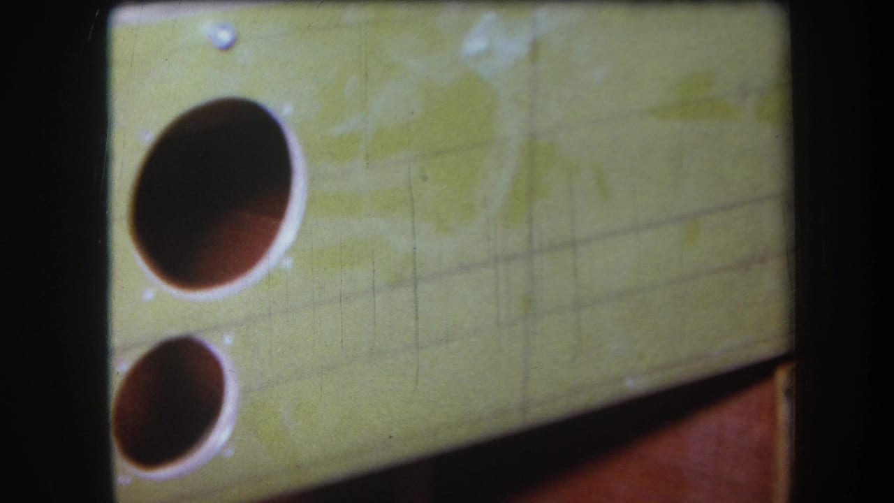 1964 8mm frame from the Yucaipa-area reel showing a yellow painted surface with two circular openings, scratches, and soft focus.