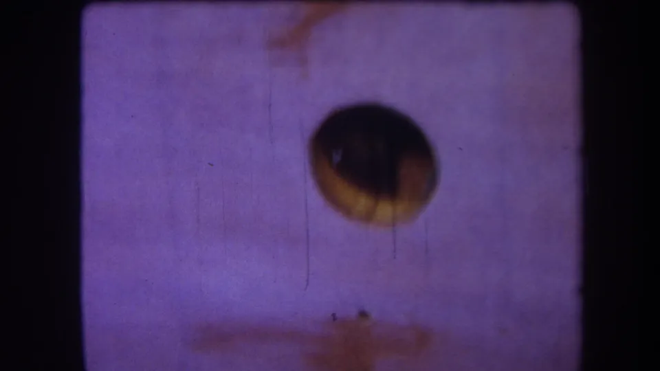 1964 8mm home-movie frame from the supplied Yucaipa reel, showing a dark circular aperture against purple faded film with scratches and dust.