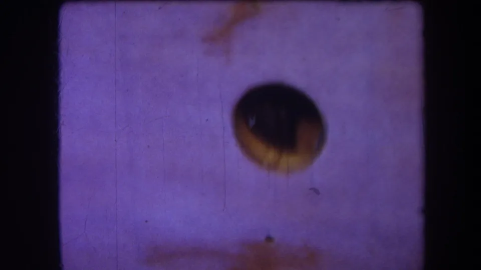 1964 Yucaipa 8mm frame with a dark aperture shape, faded purple cast, fine scratches, dust marks, and visible film-frame edges.