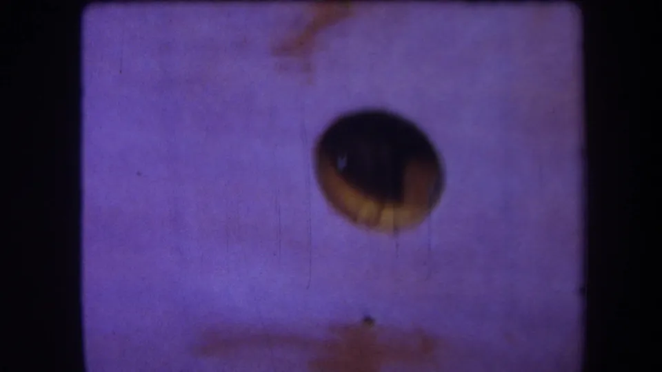 Supplied 1964 8mm frame from Yucaipa showing a soft dark aperture, purple fading, scratch lines, dust, and a brown stain near the lower edge.