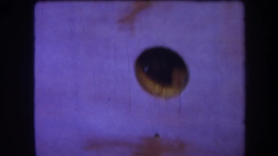 1964 Yucaipa 8mm home-movie frame with a dark circular aperture, purple color shift, dust specks, vertical scratches, and lower brown staining.