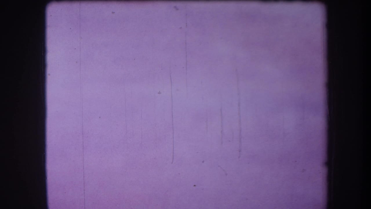 Purple-tinted blank 8mm frame with visible film grain, small dust marks, and faint vertical scratches.