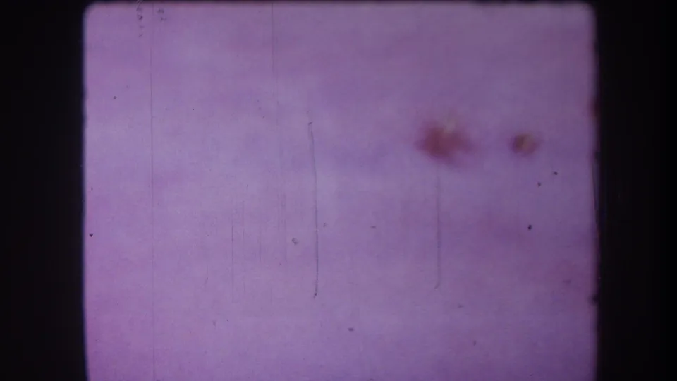 Blank purple 8mm frame from the 1964 Yucaipa reel, marked by reddish stains, dust, vertical scratches, and grain.