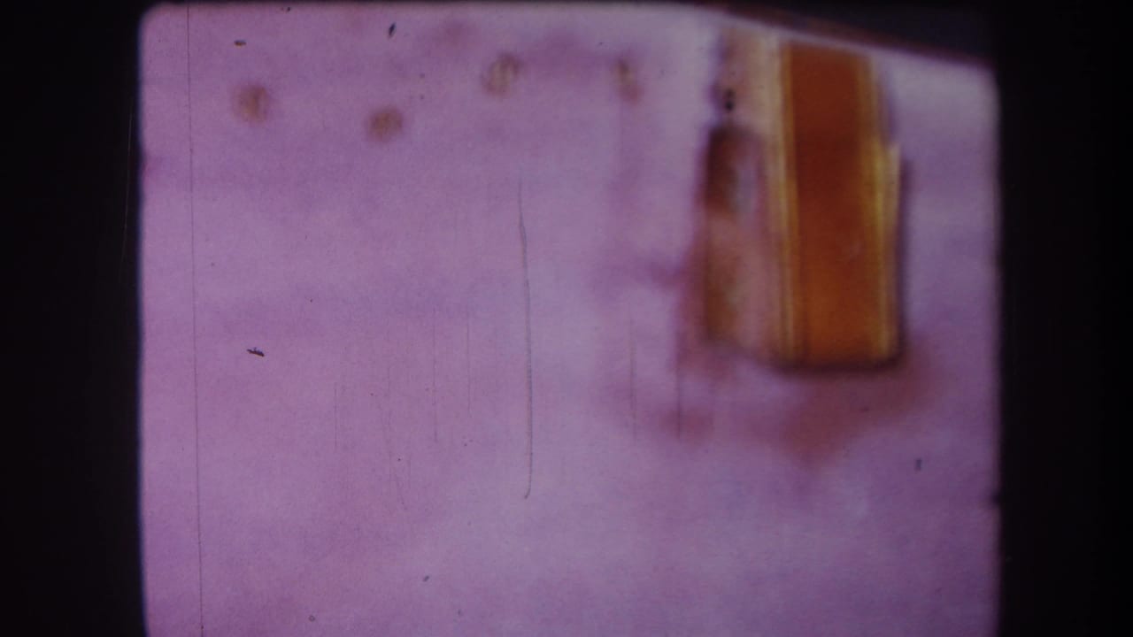 Soft-focus 1964 Yucaipa frame showing a yellow shed-like structure at right, with aged color shift, dust, scratches, and dark 8mm frame edges.