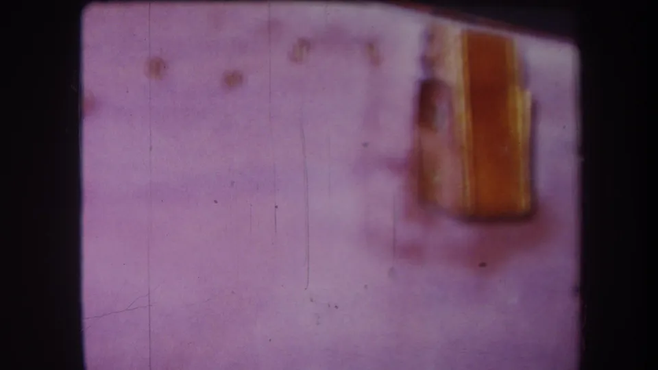 1964 Yucaipa home-movie still with the yellow shed-like structure more visible at right over a pale frozen surface, softened by aging and focus.