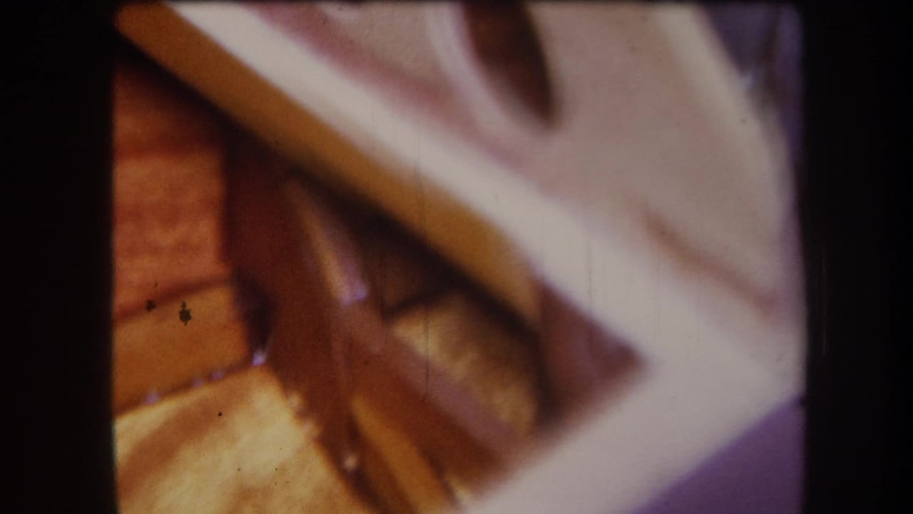 1964 Yucaipa home-movie frame showing warm wooden strips beneath a pale angled piece in a workshop close-up.