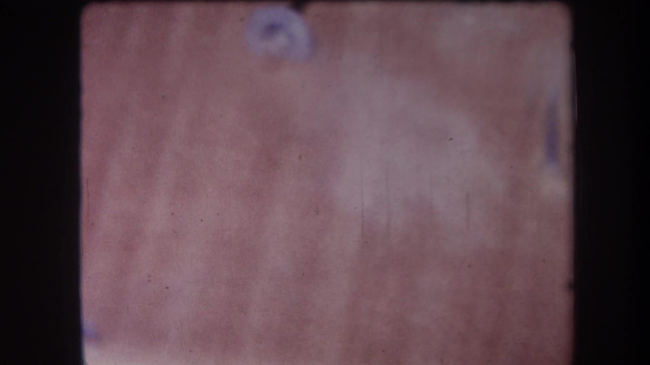 1964 Yucaipa-area 8mm frame showing a soft-focus wood surface with grain, dust marks, and dark film borders.