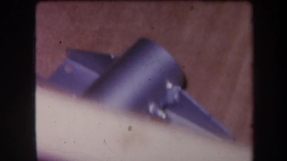 1964 Yucaipa-area close-up of metal hardware on a wood surface, softened by shallow focus and 8mm grain.