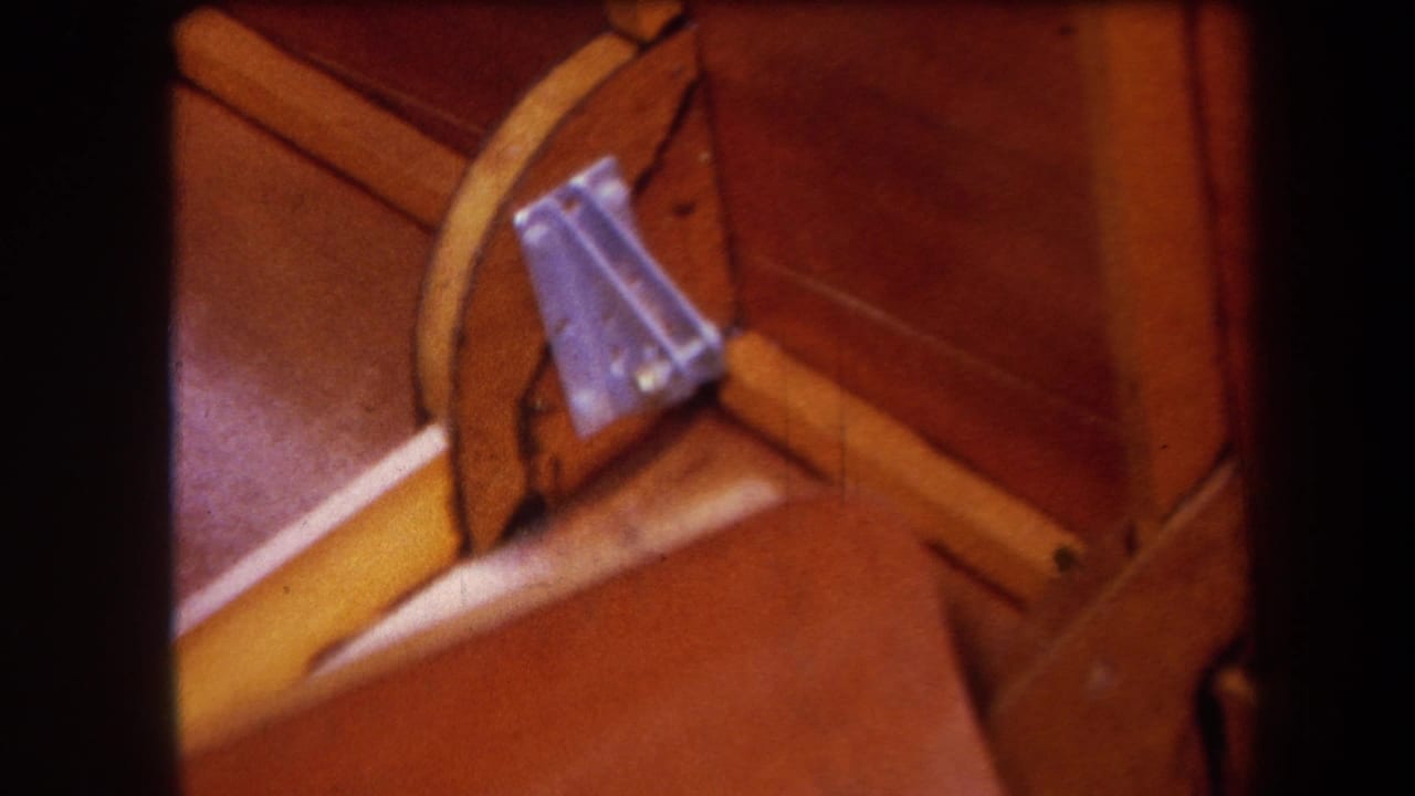 1964 Yucaipa-area 8mm close-up of a wooden mechanical structure with a yellow brace and bolted metal bracket.