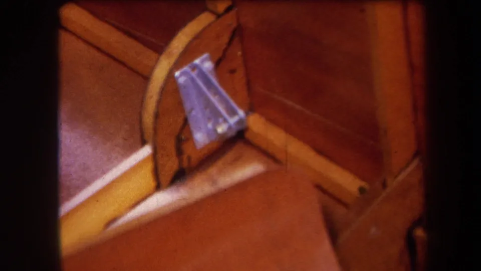 1964 Yucaipa-area 8mm close-up of a wooden mechanical structure with a yellow brace and bolted metal bracket.