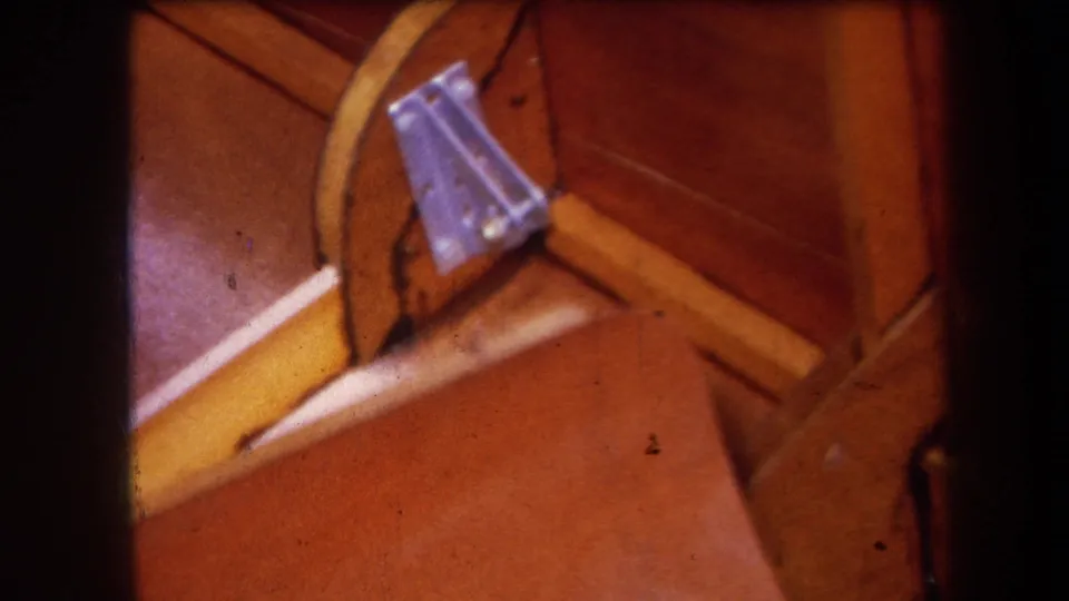Close 8mm frame of wooden machinery parts, showing a bolted metal fitting beside a yellow rail in Volmer Yucaipa footage.
