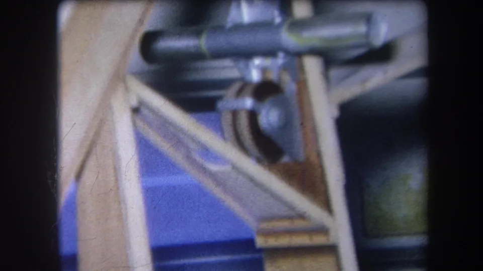 1964 Volmer Yucaipa 8mm close-up showing angled wooden framing, blue backing, and small metal machinery parts.
