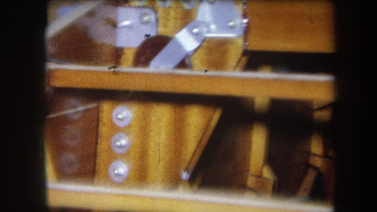Close 1964 Yucaipa frame of layered wood, metal hardware, and three circular fasteners on an unidentified mechanical object.
