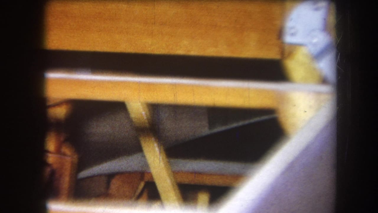 1964 8mm close-up from Yucaipa showing a wooden boat frame, angled supports, and silver metal fixtures within dark film borders.