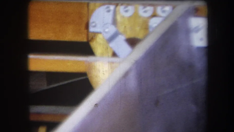 1964 8mm frame showing angled wooden supports, exterior planking, and silver bracket hardware on a small boat structure.