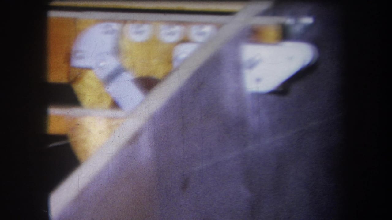 1964 8mm frame from Yucaipa metadata showing a close view of dark machinery, white brackets, yellow parts, and soft film grain.